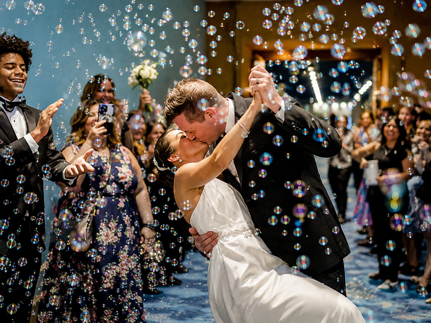 bubble - Stylus Weddings Bride and groom kiss while being spun on a dance floor, bubbles floating around guests in formal wear.