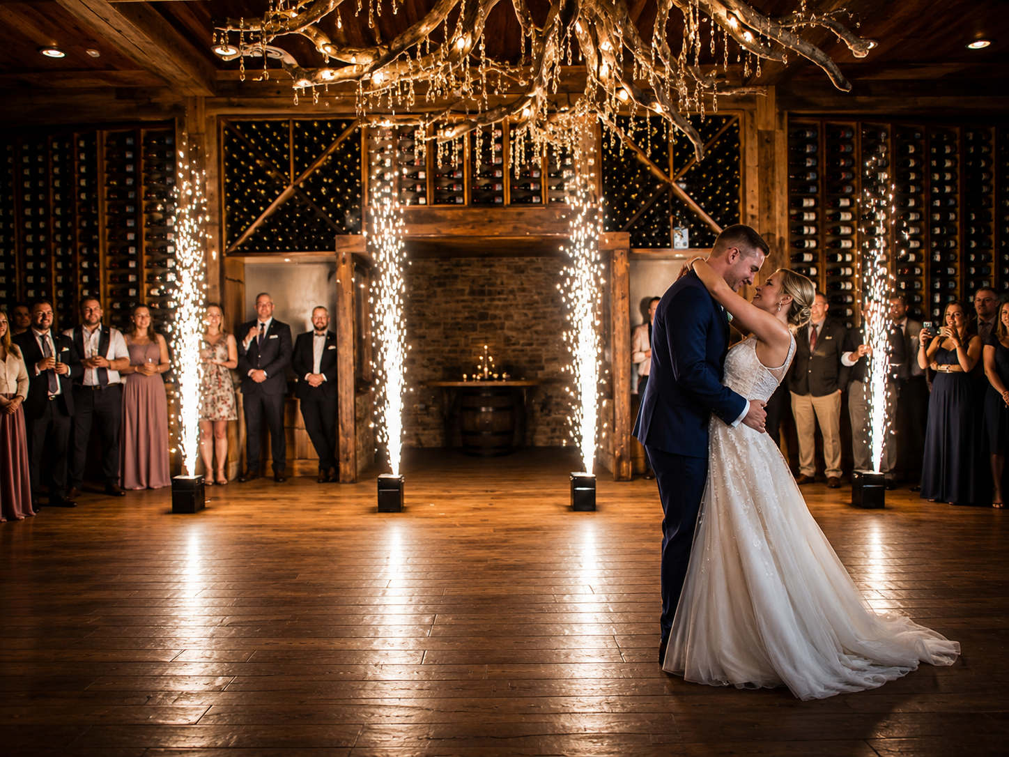 coldsparks2 - Stylus Weddings Bride and groom share a first dance in a rustic venue as sparkling fountains rise beside them and guests watch from the sides.