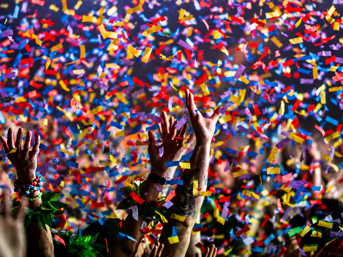 confetti - Stylus Weddings Hands raised in celebration as colorful confetti rains down on a crowd at a party.